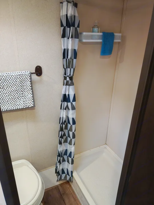 Compact RV rental bathroom featuring a toilet, geometric shower curtain, bath mat, blue towel, and sanitizer on a shelf.. Forest River Salem FSX 2018