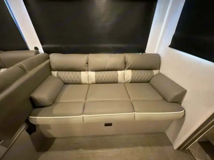 Spacious grey L-shaped sofa with patterned backs and white trim in a cozy RV rental interior, under dark window shades.. Forest River Salem Platinum 2024
