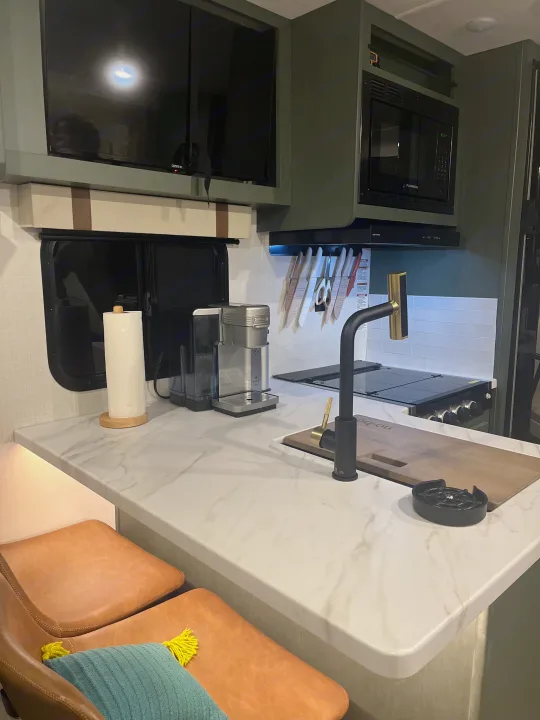 Modern RV rental kitchen featuring green cabinets, marble-look counter, coffee maker, microwave, and compact appliances.. Forest River 5NHTRDV27TD211453 2026