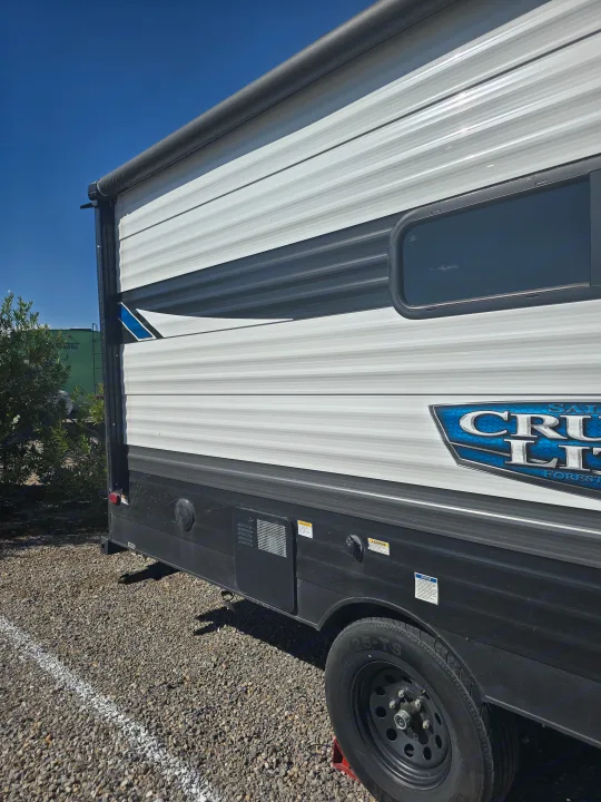 Exterior of an RV rental, a white and grey travel trailer with "CRUI LITE" branding, parked on gravel under a clear blue sky.. Forest River Salem Cruise Lite 2024