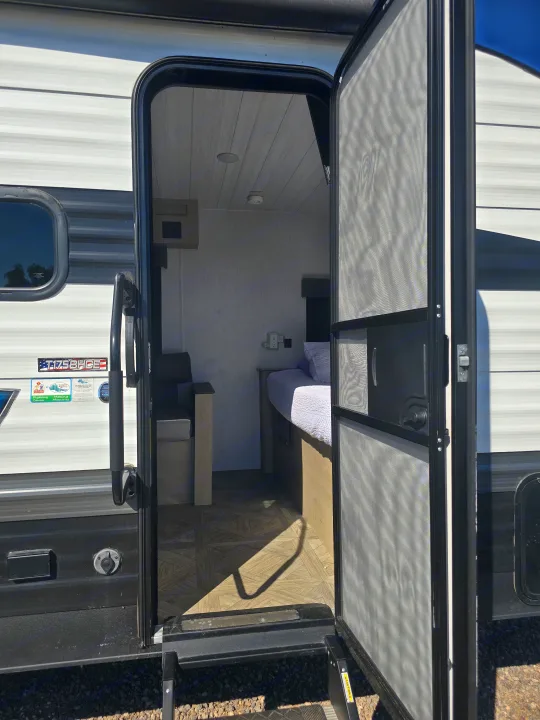 Open RV rental door showing a cozy interior with bed, dinette, and screen door. Steps lead outside.. Forest River Salem Cruise Lite 2024