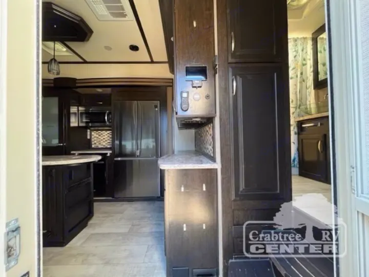 Modern RV rental interior showing a spacious kitchen with dark cabinetry, stainless steel appliances, and a peek into the bathroom.. Grand Design Momentum 2015