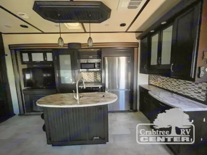 Modern RV rental kitchen with dark cabinetry, island sink, stainless steel appliances, and a living area. Stylish and spacious.. Grand Design Momentum 2015