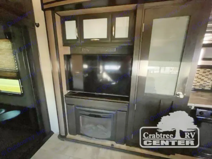 RV rental interior: cozy living space with a TV, electric fireplace, dark wood cabinets, and a stylish glass door.. Grand Design Momentum 2015