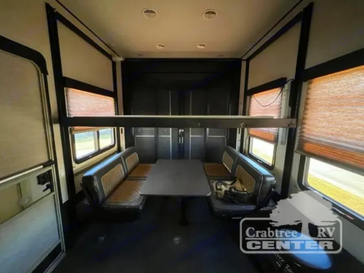 Spacious RV rental interior: A dining area with dark benches & table, plus a raised bunk bed above. Bright windows with blinds.. Grand Design Momentum 2015
