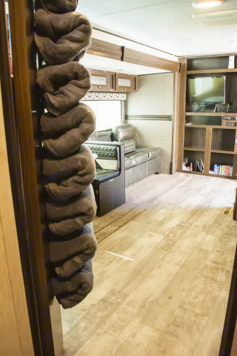 RV rental living area: A cozy space with a dark leather sofa, TV, and rolled towels hanging by the entrance.. Heartland RVs Pioneer 2019