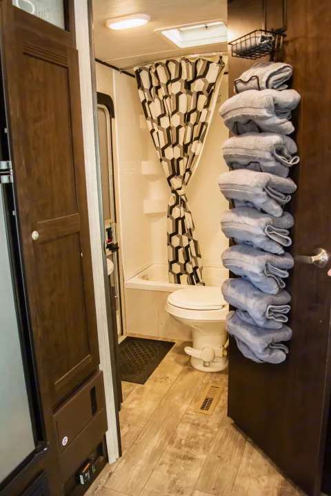 An efficient RV rental bathroom featuring a shower, toilet, and neatly stacked towels on a door organizer.. Heartland RVs Pioneer 2019