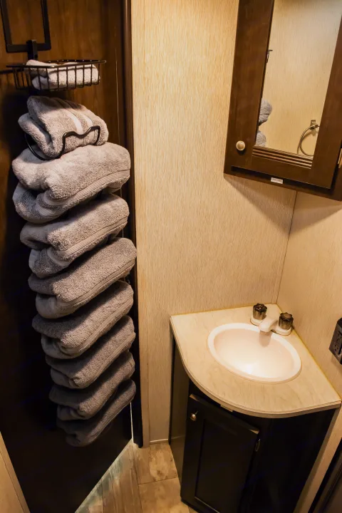 RV rental bathroom featuring stacked grey towels, a corner sink vanity, and a mirrored medicine cabinet. Essential amenities for comfortable travel.. Heartland RVs Pioneer 2019