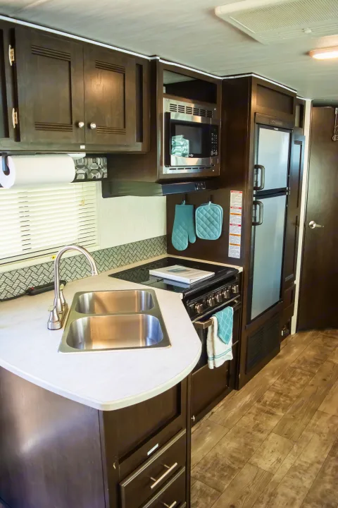 RV rental kitchen: double sink, stove, microwave, fridge, dark cabinets, light counters, and wood-look floor.. Heartland RVs Pioneer 2019