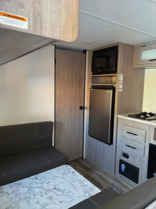 RV rental: interior view of a bright kitchen and dinette, featuring microwave, fridge, stovetop, and bench seating.. Dutchmen Kodiak Cub 2024