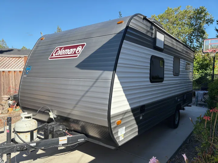 This gray Coleman travel trailer RV rental, parked on concrete, awaits its next adventure. Perfect for camping trips!. Dutchmen Kodiak Cub 2024