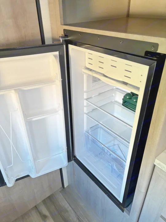 This open mini-fridge in an RV rental offers convenient cold storage with clean shelves, door storage, and a small freezer.. Dutchmen Kodiak Cub 2024