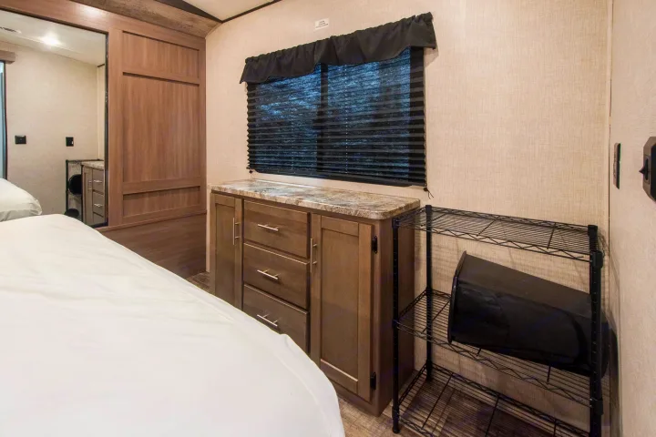 RV rental bedroom featuring a bed, mirrored wardrobe, dresser with a counter, window, and wire storage shelves.. Crossroads RV Sunset Trail 2022