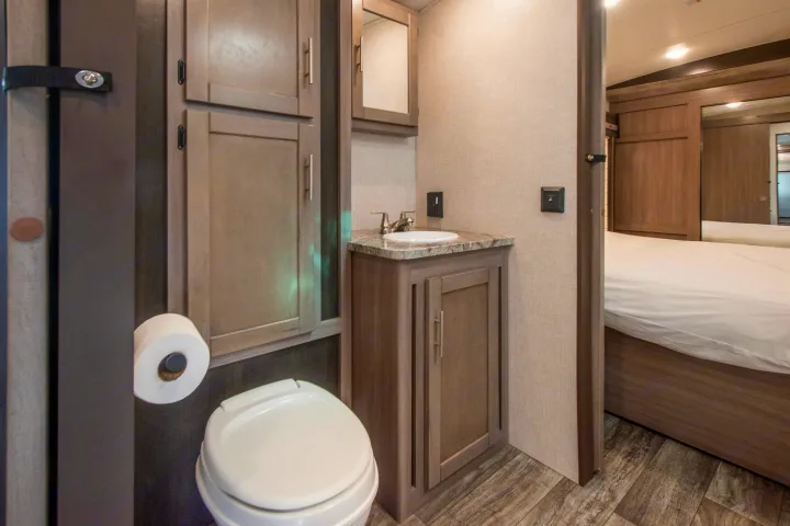 This RV rental features a compact bathroom with a toilet, sink, and cabinets, opening to a cozy bedroom area with a bed.. Crossroads RV Sunset Trail 2022
