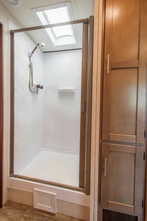 Clean RV rental bathroom showcasing a modern shower with a skylight and wood cabinets for your next trip.. Crossroads RV Sunset Trail 2022