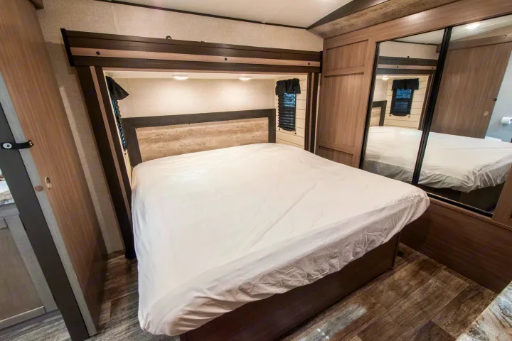 RV rental bedroom with a neatly made bed, built-in lighting, wood-look flooring, and mirrored closet doors.. Crossroads RV Sunset Trail 2022