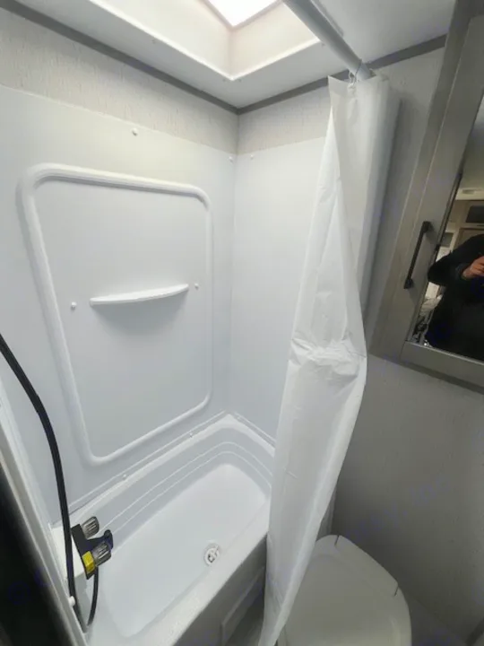 Compact RV rental bathroom featuring a shower-tub combo, white shower curtain, and a skylight for brightness.. Dutchmen Kodiak Cub 2022