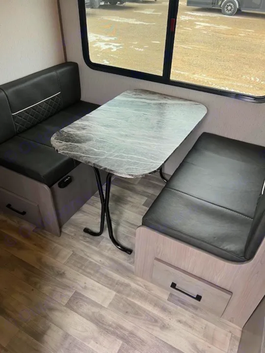 Inside this RV rental, a cozy dinette features black leatherette benches, a light patterned table, window views, and wood-look flooring.. Dutchmen Kodiak Cub 2022