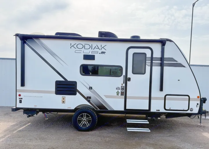 White Kodiak Cub travel trailer, ideal for your next RV rental adventure, parked on gravel under a cloudy sky.. Dutchmen Kodiak Cub 2022