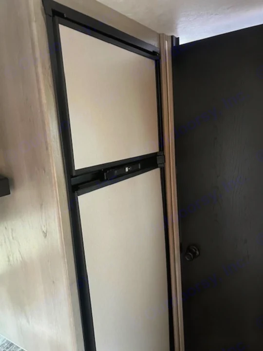 RV rental: Compact, two-door refrigerator with a control panel, integrated into wood-paneling next to a black door.. Dutchmen Kodiak Cub 2022