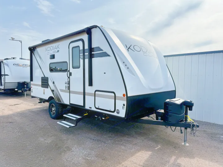 A white Kodiak Cub travel trailer, ready for adventure and perfect for an rv rental, parked on gravel under a bright, partly cloudy sky.. Dutchmen Kodiak Cub 2022