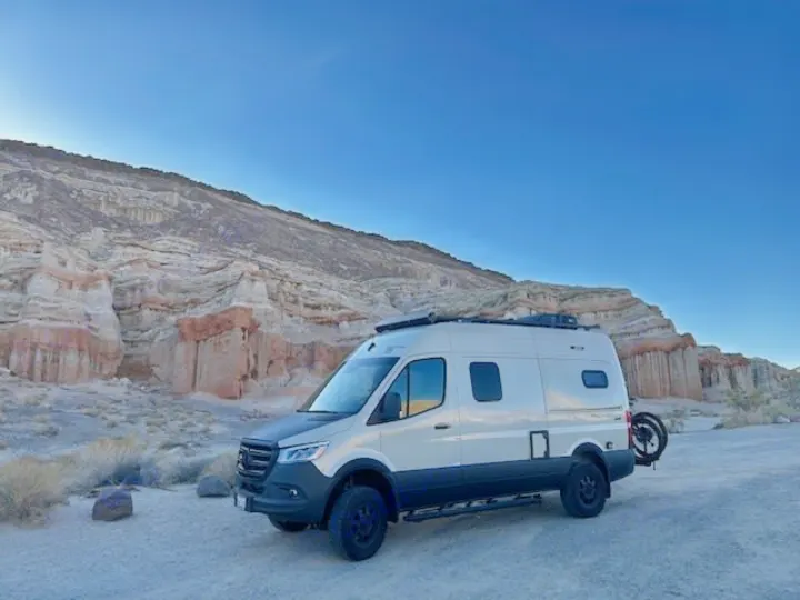 RV rental van, cream-colored, parked at unique desert rock formations under a clear sky, ready for your next adventure.. Winnebago Revel 2024