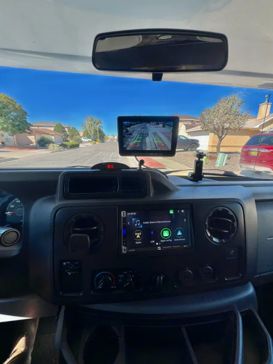 View from an RV rental driver's seat showing dashboard, backup camera display, and infotainment system on a sunny street.. Thor Majestic 2019