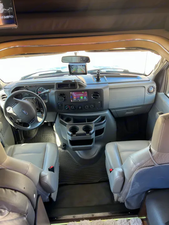 RV rental interior: Front cabin with dashboard, steering wheel, driver/passenger seats, and infotainment system.. Thor Majestic 2019