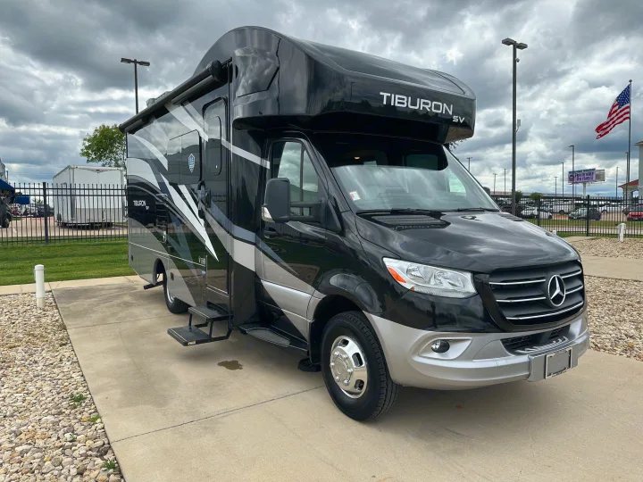 A stylish black & silver Mercedes-Benz RV, labeled 'Tiburon SV,' parked under a cloudy sky. Ideal for your next rv rental.. Thor Tiburon SV 2023