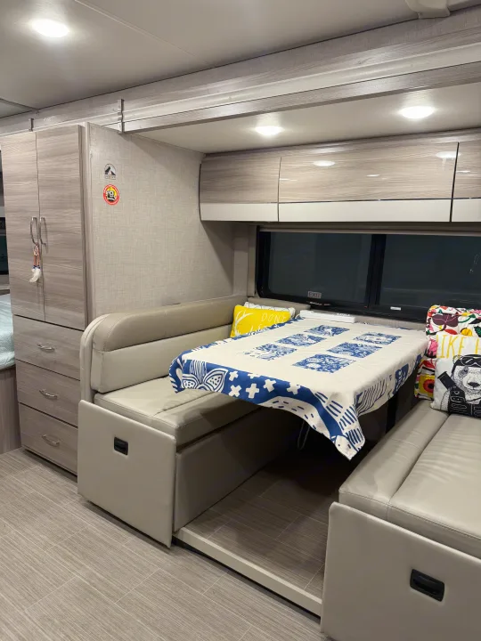 This rv rental shows an inviting dinette with a blue and white patterned tablecloth, wood-grain cabinets, and comfortable seating.. Thor Tiburon SV 2023