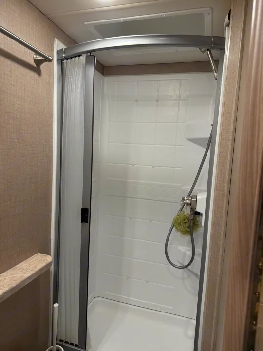 Clean, compact RV rental shower featuring a curved rod, tiled-look enclosure, and flexible shower head.. Thor Tiburon SV 2023