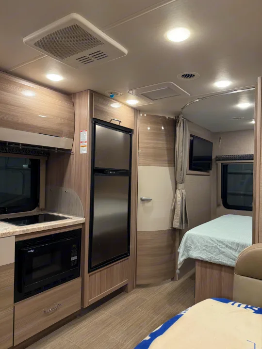 Spacious and modern rv rental interior showcasing a kitchenette, fridge, bed, and ceiling vents for comfort.. Thor Tiburon SV 2023