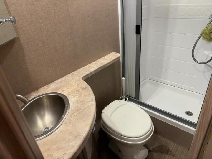 RV rental bathroom features a compact sink, white toilet, and shower stall. Textured walls and wood-look flooring.. Thor Tiburon SV 2023