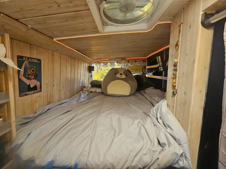 Cozy RV rental interior with wooden walls, a ceiling fan, LED lights, a plush toy on a bed, and a "Be Kind" sign.. Dodge 159 3500 2022