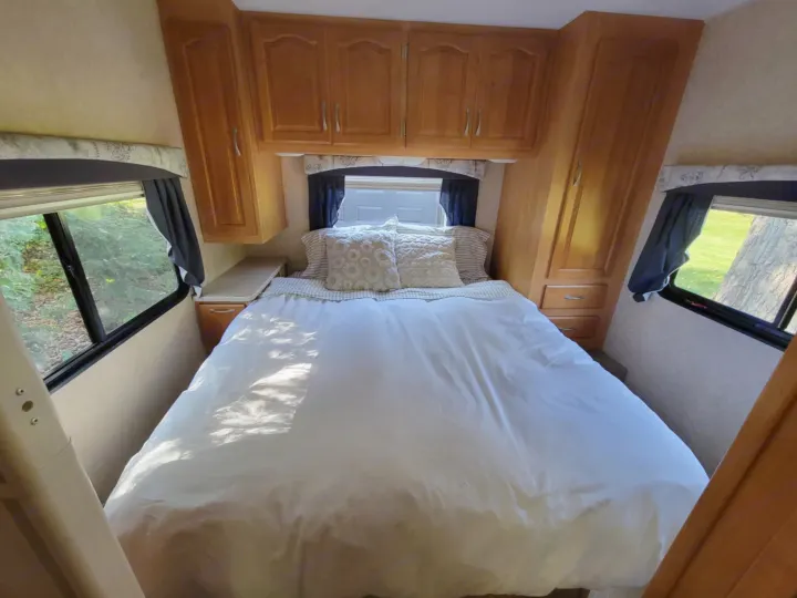Cozy RV rental bedroom with a comfortable bed, wooden cabinets, and large windows offering scenic outdoor views.. Forest River Sunseeker LE 2006