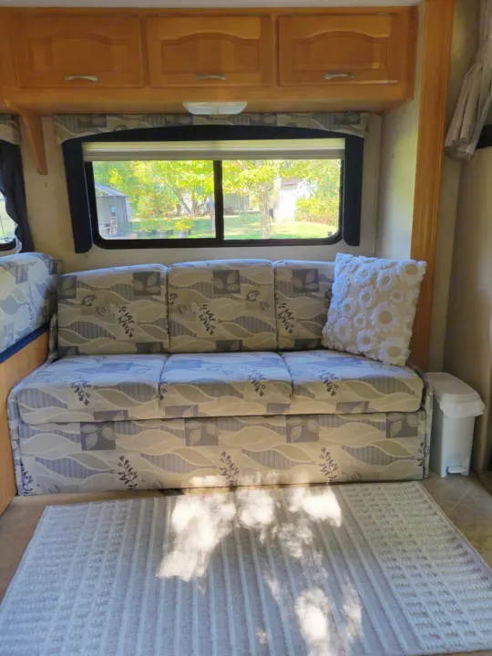 RV rental interior with a patterned sofa, decorative pillow, window view, and wooden cabinets.. Forest River Sunseeker LE 2006