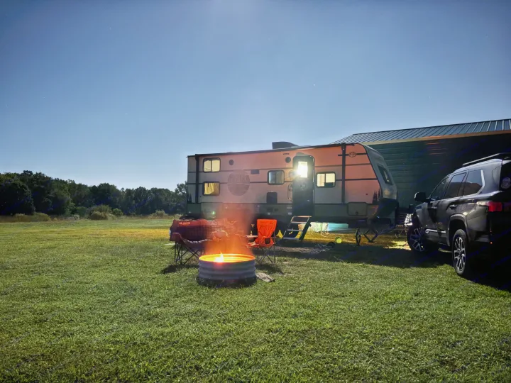 An RV rental setup at night: travel trailer, SUV, warm campfire, and chairs under a starry sky in a grassy field.. Forest River 5NHTRDV27TD211453 2026