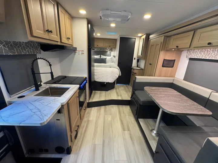 Step inside this modern rv rental: kitchen with stove, sink, and an L-shaped dinette, leading to a cozy bedroom.. Forest River Sunseeker 2026
