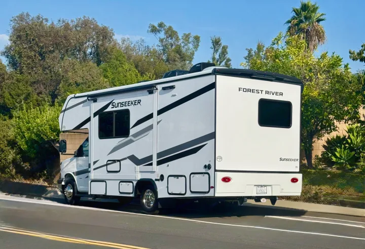 This white Forest River Sunseeker RV rental, a Class C motorhome, is parked on a sunny road with green trees.. Forest River Sunseeker 2026