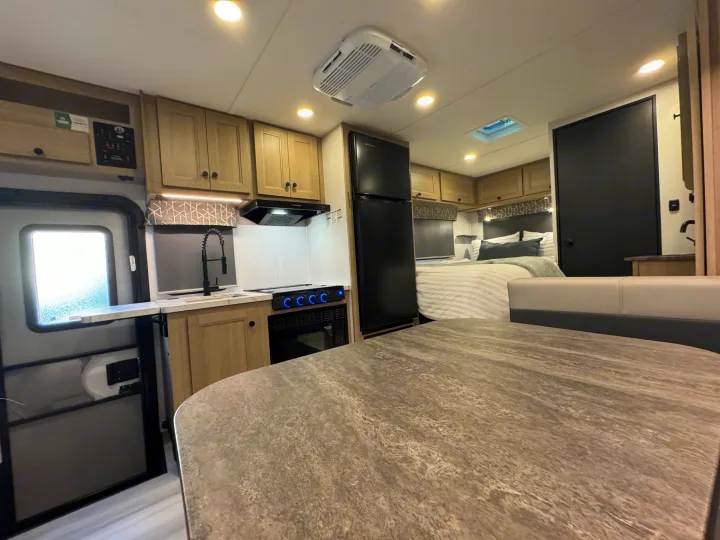 Modern RV rental interior showing a full kitchen, comfortable sleeping area, and a gray dining table.. Forest River Sunseeker 2026