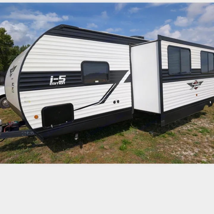 White and black travel trailer RV, an rv rental, with an extended slide-out panel on grass. Features 'I-5 EDITION' & 'Shasta' branding.. Coachmen I-5 Edition 530QB 2024