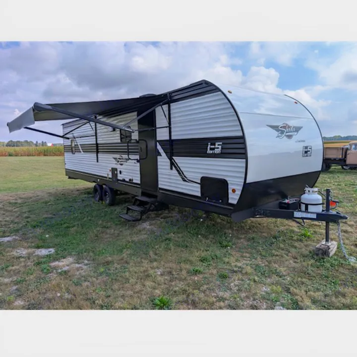 Shasta I-5 Edition travel trailer, a white and black RV rental unit with an extended awning, parked on a grassy field under a cloudy sky.. Coachmen I-5 Edition 530QB 2024