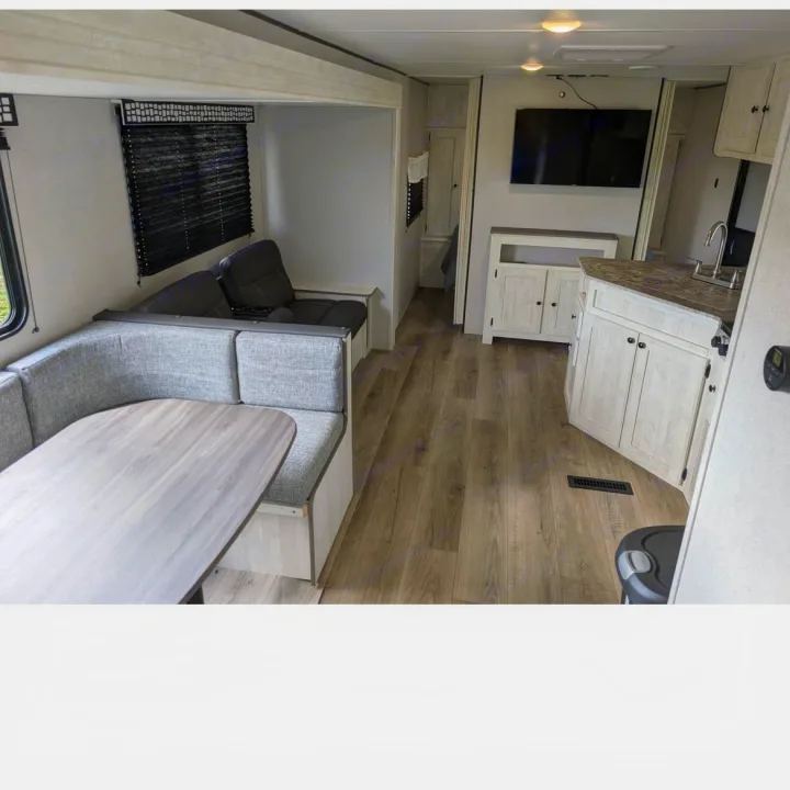 Bright RV rental interior featuring a dining booth, sofa, TV, and kitchen with light wood-look flooring.. Coachmen I-5 Edition 530QB 2024