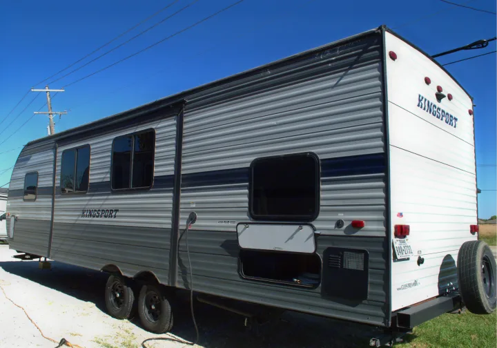 Kingsport travel trailer RV rental exterior, a gray unit parked outdoors. Features storage, power hookup, and rear spare tire.. Gulf Stream Kingsport 2021