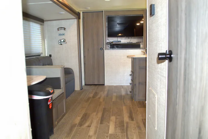 Cozy rv rental interior featuring a dinette, sofa, wall-mounted TV, soundbar, and a sink vanity with wood-look flooring.. Gulf Stream Kingsport 2021