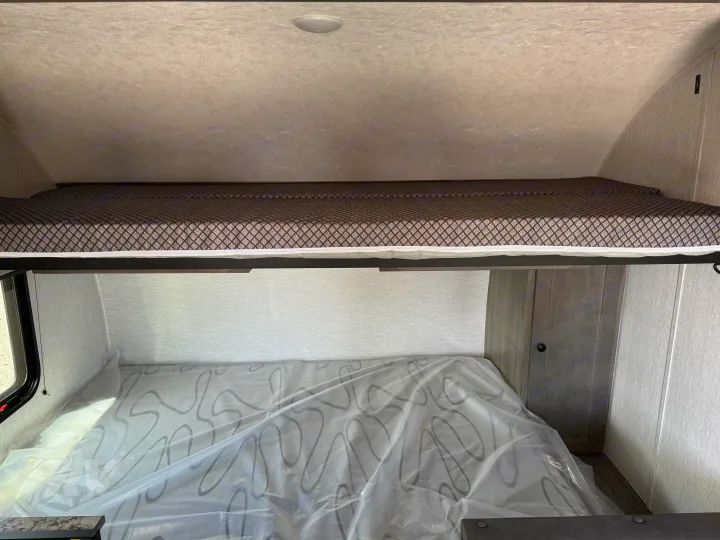 RV rental: Upper bunk bed with patterned mattress, lower bed covered in protective plastic, ready for your adventure.. Sunlite 16BH 2025