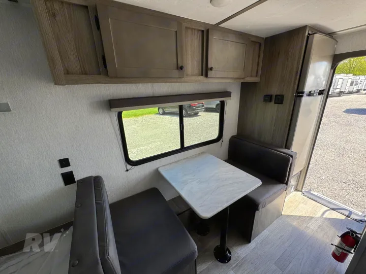 This rv rental's interior features a compact dinette with a window, overhead cabinets, and a refrigerator by the entry.. Sunlite 16BH 2025