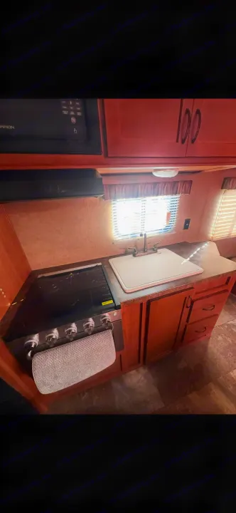 Equipped RV rental kitchen features a microwave, 4-burner stove, sink, and wooden cabinets for convenient cooking.. Forest River Cherokee Grey Wolf 2014
