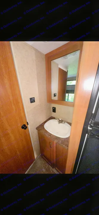 RV rental bathroom vanity featuring a sink, mirror, and wood cabinet. Functional, compact space next to a wooden door.. Forest River Cherokee Grey Wolf 2014