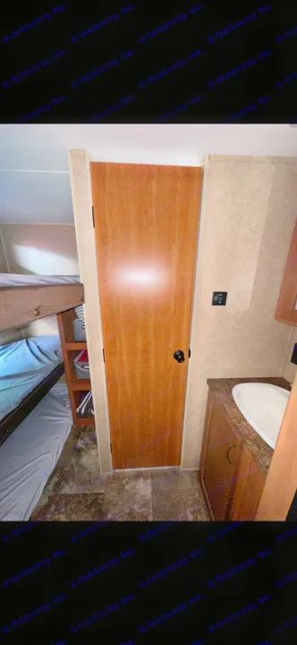 Compact rv rental interior with bunk beds, a wooden door, and a small sink vanity on the right.. Forest River Cherokee Grey Wolf 2014